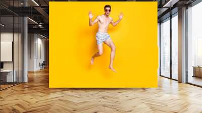 Photo of charismatic funky young man naked torso wear dark eyewear jumping high smiling isolated yellow color background Wall mural