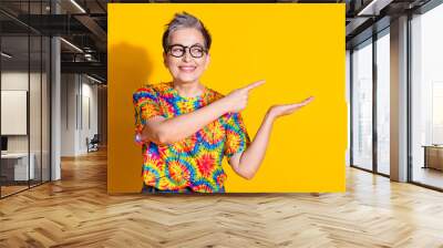 Photo of charming adorable senior woman wear stylish print clothes look empty space isolated on yellow color background Wall mural