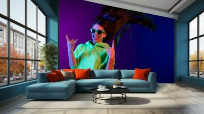 Photo of charming crazy young woman make rock sings stick out tongue fly hair isolated on neon color background Wall mural