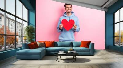 Photo of charming dreamy man wear blue hoodie looking empty space rising paper heart isolated pink color background Wall mural