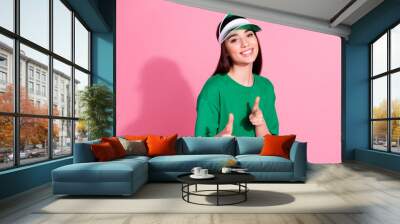 Photo of charming positive woman wear green t-shirt cap pointing you two fingers empty space isolated pink color background Wall mural