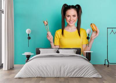 Photo of charming young lady wear yellow crop top holding beef burger sushi roll isolated turquoise color background Wall mural