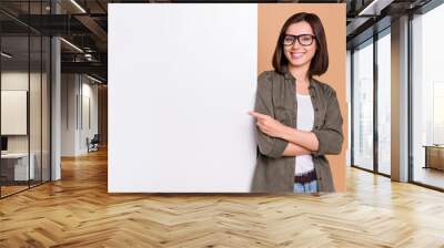 Photo of cheerful lady direct forefinger placard board empty space wear specs khaki shirt isolated beige color background Wall mural