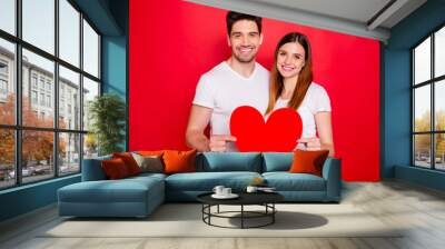 Photo of cheerful positive pretty cute nice couple of spouses holding big red white t-shirt heart smiling toothily showing their love isolated vivid color background Wall mural