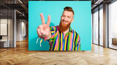 Photo of cheerful satisfied positive glad man wear trendy colorful striped clothes show two fingers v-sign isolated on cyan color background Wall mural