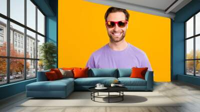 Photo of cheerful traveler guy toothy beaming smile wear sunglass purple t-shirt isolated yellow color background Wall mural