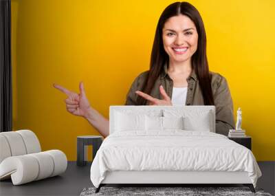 Photo of cheerful young charming woman point fingers empty space indicate news isolated on yellow color background Wall mural