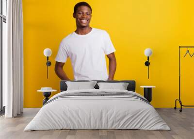 Photo of cheerful young dark skin happy man hold hands jeans pockets isolated on shine yellow color background Wall mural