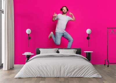 Photo of confident reliable guy jump raise two thumbs up wear striped t-shirt jeans sneakers isolated pink color background Wall mural