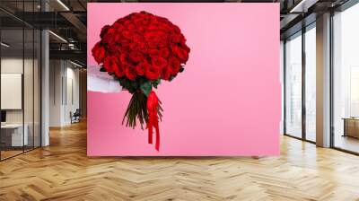 Photo of cropped man arms hold big one hundred red bright roses bunch giving secret admirer delivery service worker valentine day romance concept isolated pink color background Wall mural