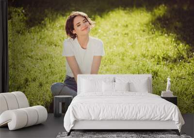 Photo of cute charming lady sitting lend ground fresh green grass enjoy sun rays eyes closed nature harmony student resting from city crowd people wear t-shirt jeans colorful park outdoors Wall mural