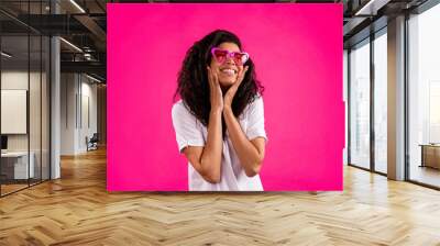 Photo of cute curly millennial lady look empty space wear spectacles white t-shirt isolated on pink color background Wall mural