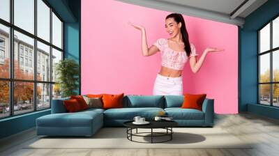 Photo of cute young brunette lady hold empty space wear crop top jeans isolated on pink color background Wall mural