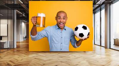 Photo of dark skin amazed guy hold hands ball beer glass support team yelling loud wear jeans denim shirt isolated bright yellow background Wall mural