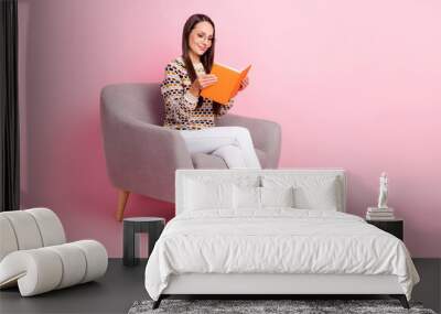 Photo of dreamy shiny young woman wear dotted sweater smiling sitting armchair reading book empty space isolated pink color background Wall mural