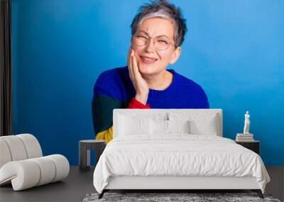 Photo of elderly charming woman wear stylish clothes touch face isolated on blue color background Wall mural