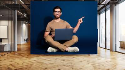 Photo of engineer brunet man sitting with laptop working directing finger empty space new technology isolated on dark blue color background Wall mural