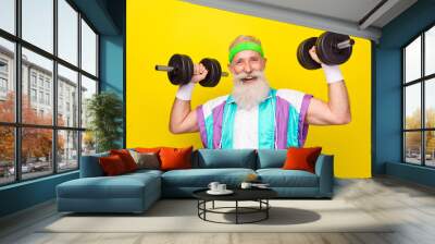 Photo of excited cheerful granddad toothy smile hands hold lift dumbbells isolated on yellow color background Wall mural