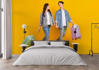 Photo of excited funny married couple wear jeans holding hands going new journey isolated yellow color background Wall mural