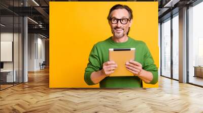 Photo of funny dreamy guy hold tablet look up empty space wear eyewear green sweater isolated yellow color background Wall mural