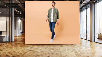 Photo of funny handsome young gentleman wear khaki shirt walking laughing smiling isolated beige color background Wall mural