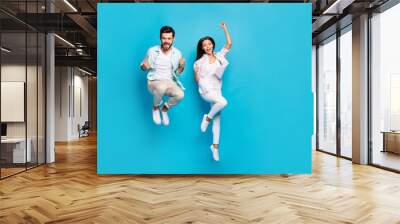 Photo of funny lucky young lovers dressed casual shirts jumping high rising fists isolated blue color background Wall mural