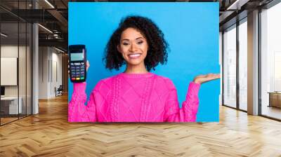 Photo of girlish lovely lady pink knitwear smiling holding payment machine showing arm empty space isolated blue color background Wall mural