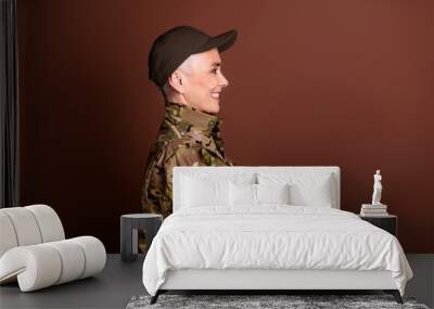 Photo of good mood confident retired woman wear camouflage arms crossed looking empty space isolated brown color background Wall mural