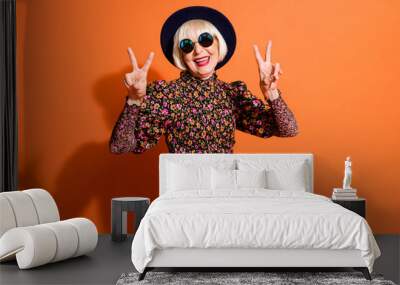 Photo of good mood happy smiling positive old woman show v-sign wear sunglasses black headwear isolated on orange color background Wall mural