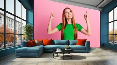 Photo of gorgeous woman with ginger hair dressed green t-shirt directing look up at logo empty space isolated on pink color background Wall mural