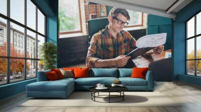 Photo of handsome young man wear checkered shirt sit table workplace read stats indoors office loft interior Wall mural