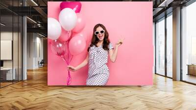 Photo of impressed cute woman wear white dress dark glasses showing v-sign holding balloons isolated pink color background Wall mural