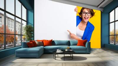 Photo of impressed funky lady dressed blue blazer eyewear pointing white wall placard empty space isolated yellow color background Wall mural