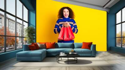 Photo of impressed funny woman with perming coiffure dressed striped sweater holding shopping bags isolated on yellow color background Wall mural