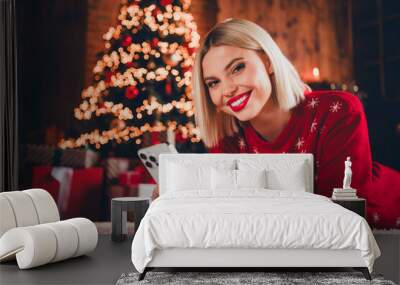 Photo of nice young blonde girl hold gadget lying floor wear christmas sweater enjoy cozy x-mas party decoration interior flat indoors Wall mural