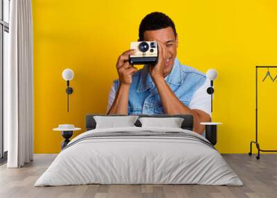 Photo of optimistic guy dressed jeans waistcoat holding retro camera on eye make photo isolated on vibrant yellow color background Wall mural