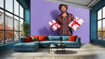 Photo of optimistic nice man with wavy hair dressed print shirt holding two gift boxes on birthday isolated on purple color background Wall mural