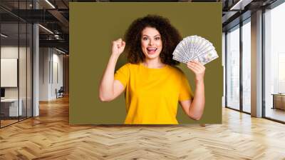 Photo of overjoyed woman in yellow t shirt basic clothes raised fist up winning lottery ticket money isolated on khaki color background Wall mural