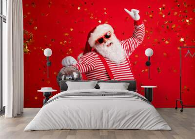 Photo of pensioner old man grey beard hold retro disco ball dance raise finger wear santa x-mas costume suspenders sunglass gloves striped shirt cap isolated red color background Wall mural