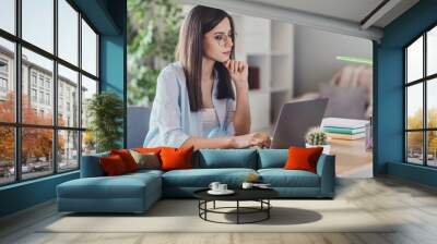 Photo of pensive young lady sit desktop finger chin look laptop calm face wear eyeglasses shirt in home office indoors Wall mural