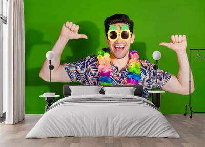 Photo of perky funny guy with bristle dressed print shirt in sunglass necklace indicating at himself isolated on green color background Wall mural