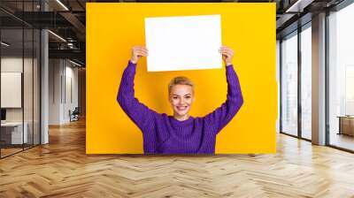 Photo of positive adorable lady wear trendy clothes arms up hold paper empty space presenting novelty isolated on yellow color background Wall mural