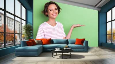 Photo of positive cheerful pretty lady dressed striped clothes shiny bright grin arm show empty space isolated on green color background Wall mural