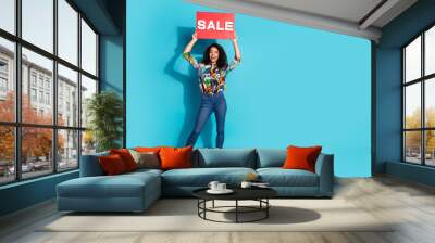 Photo of positive glad lovely cute girl wear stylish outfit showing red poster sale proposition empty space isolated on blue color background Wall mural