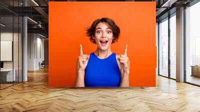 Photo of positive impressed lady wear blue singlet open mouth pointing two fingers up empty space isolated orange color background Wall mural