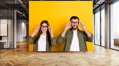 Photo of positive intelligent woman and man wear eyeglasses look up see promotion ad isolated on yellow color background Wall mural