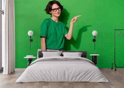 Photo of positive lady look direct finger empty space offer promo isolated on green color background Wall mural