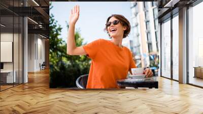 Photo of positive lovely girl dressed stylish outfit sitting in cafe drinking morning beverage meeting best friend saying hi Wall mural