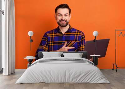 Photo of positive man indicate finger hand hold laptop beaming smile isolated on orange color background Wall mural