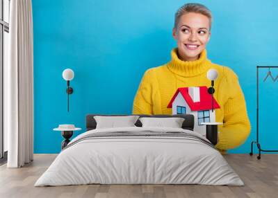 Photo of positive new ownership cute blonde short hair girl wear yellow jumper look empty space hold house no loan isolated on blue color background Wall mural